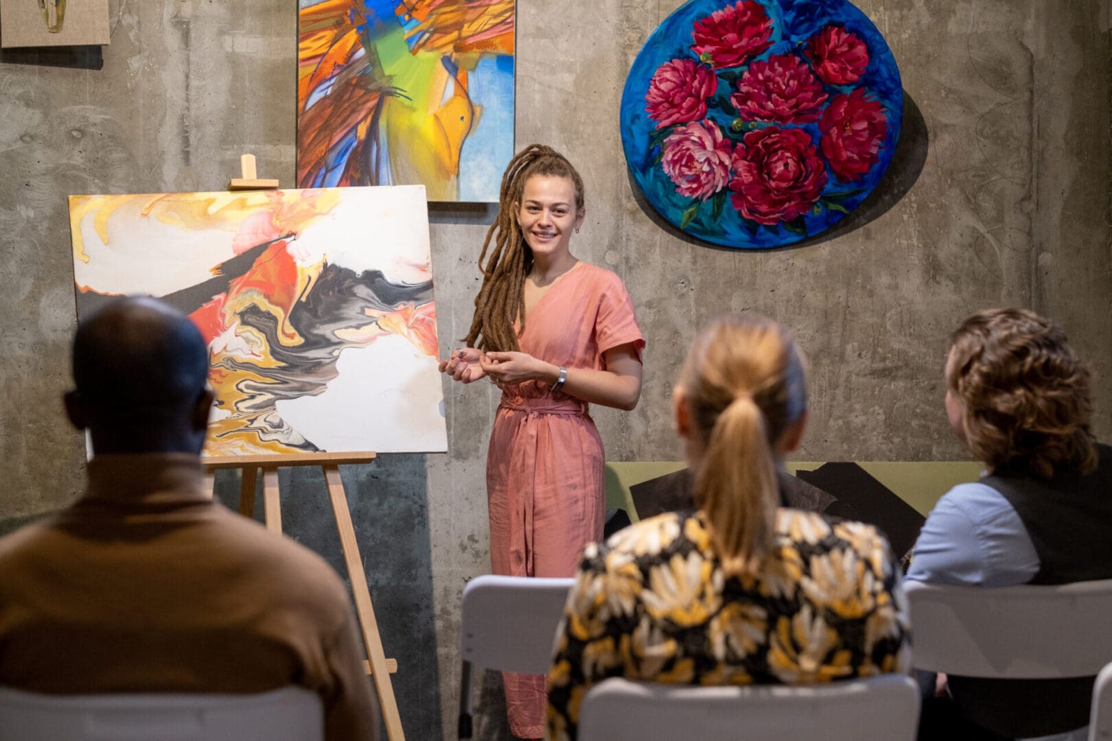 Happy young female auctioneer presenting abstract painting to audience before starting sale auction